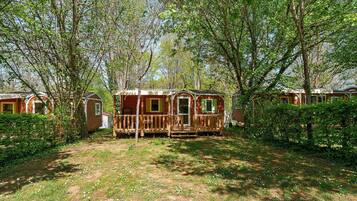 A wooden cabin with a porch, surrounded by trees and a grassy area.