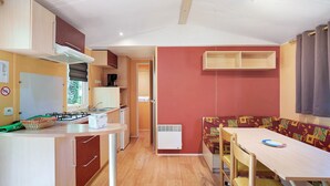 Une petite cuisine équipée avec une cuisinière, un évier et des placards, un coin repas avec une table et des chaises, et un mur d’accent de couleur rouge.