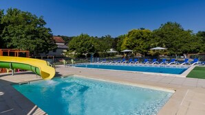 Une piscine avec un toboggan, des chaises longues et des parasols.
