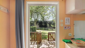 Une terrasse en bois qui mène à un jardin offrant une vue sur les arbres et une pelouse.
