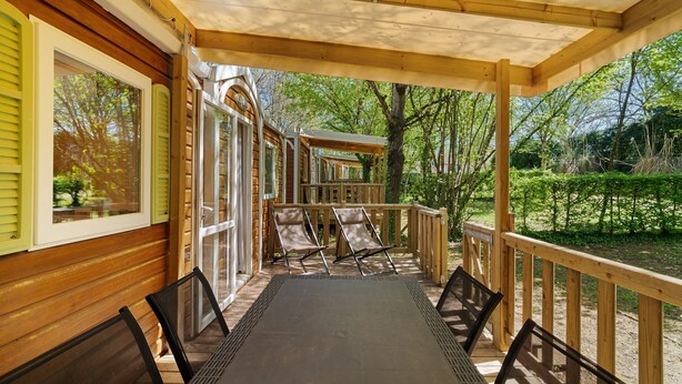 Una terraza cubierta al aire libre con una mesa y sillas, barandillas de madera y vistas del entorno verde.