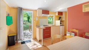 Una cocina compacta con estufa a gas, microondas y lavamanos, una mesa de comedor con sillas y vistas al exterior.