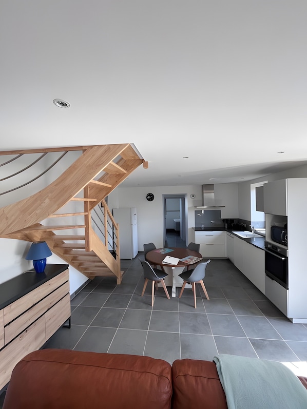 Une cuisine moderne avec un coin repas, un escalier en bois et un canapé.