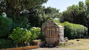 Una costruzione in pietra con un cancello in legno, circondata da vegetazione lussureggiante e un vialetto sterrato.