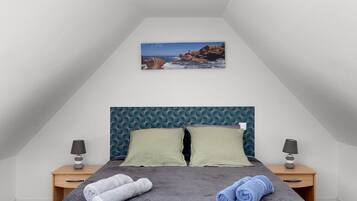 A bedroom with a bed, two pillows, two bedside tables with lamps, and a painting of a rocky coastline.