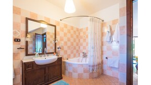 Een badkamer met een wastafel, wastafelmeubel, spiegel, douche en betegelde wanden.