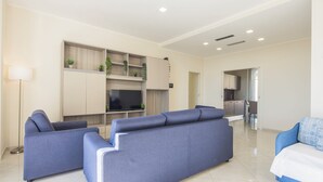 A modern living room with a sofa set, a flat-screen TV, and a kitchen area in the background. - Luxury Seafront Apartment Private Terrace Crescent (Salerno)