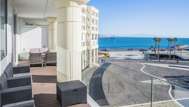 A balcony with wicker furniture, a view of the sea, and a promenade with palm trees. - Luxury Seafront Apartment Private Terrace Crescent (Salerno)