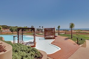 A pool area with wooden pergolas, a curved deck, and a view of the ocean. - NEW Beach Apartment in Quarteira (Loulé)