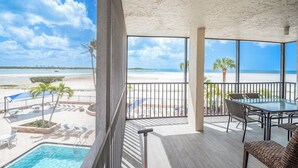 A balcony with a pool, beach view, and outdoor seating. - SUMMER DISCOUNT! Beachfront 2B/2B Vacation Condo Carlos Pointe 221. Amazing Views! EVERYTHING BRAND NEW! (Fort Myers Beach)