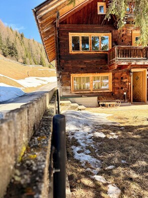 Una baita di legno con un balcone, ampie finestre e un vialetto in pietra che conduce all'ingresso.