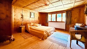 Une chambre dans une cabane en bois, avec un lit, une fenêtre avec des rideaux, un radiateur et une chaise.