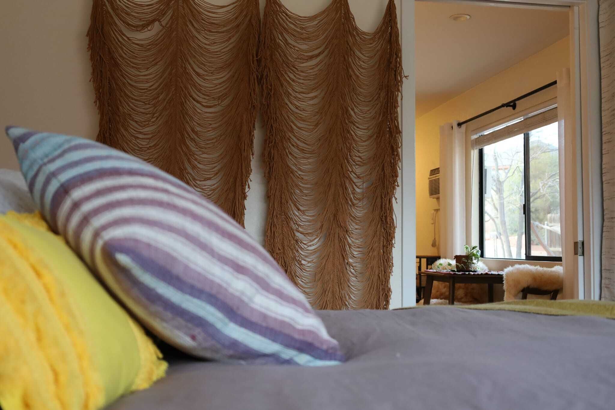 Een slaapkamer met een bed, gestreepte kussens en uitzicht op het landschap door een raam.