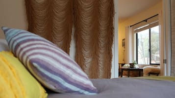 Een slaapkamer met een bed, gestreepte kussens en uitzicht op het landschap door een raam.
