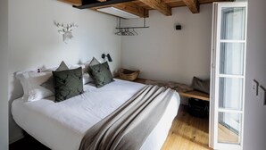 Ein Schlafzimmer mit Holzbalkendecke, einem Bett mit weißer Bettwäsche und grünen Kissen, einer kleinen Bank und einem Fenster.