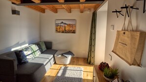 Ein gemütliches Wohnzimmer mit Holzbalkendecke, einem grauen Sofa, einem weißen Couchtisch und einem Gemälde einer Berglandschaft.
