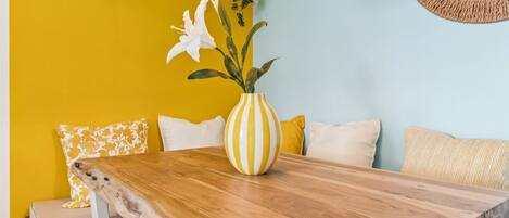 A wooden table with a striped vase, yellow and white pillows, and a white chair.
