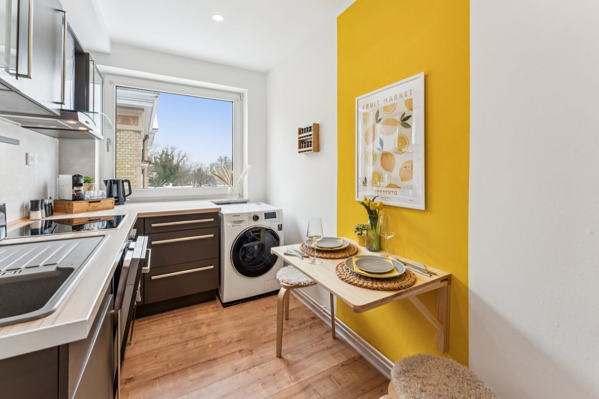 A compact kitchen with modern appliances, a dining area with yellow walls, and a large window providing a view of the outside.