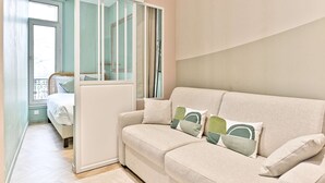 A modern living room with a sofa, cushions, and a sliding glass door leading to a balcony. - Charmant, confortable et climatisé - Paris 17 (Paris)