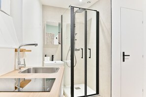 A modern bathroom with a glass-enclosed shower, a sink, and a mirror. - Studio tout confort climatisé – proche métro (Paris)