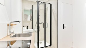 Une salle de bain moderne avec une douche à parois de verre, un lavabo doté d’un robinet contemporain et une porte blanche.