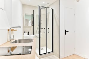 A modern bathroom with a glass-enclosed shower, a sink with a modern faucet, and a white door. - Studio tout confort climatisé – proche métro (Paris)