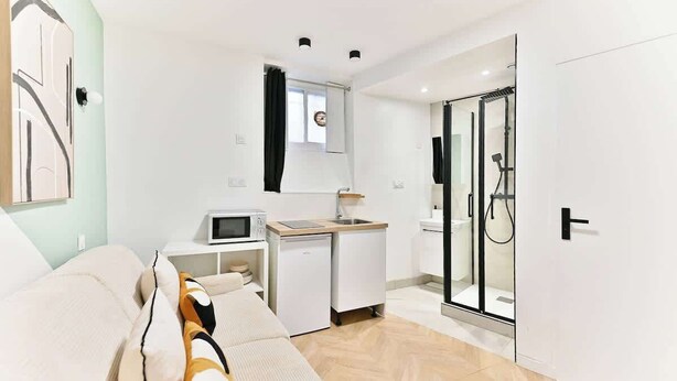 Une chambre d’hôtel moderne équipée d’un canapé, d’une petite kitchenette, d’une douche à parois de verre et d’une porte.
