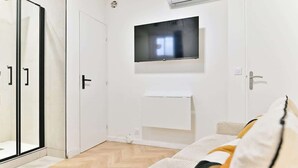 Une chambre moderne dotée d’un grand miroir, d’un téléviseur à écran plat fixé au mur et d’un canapé avec des coussins.