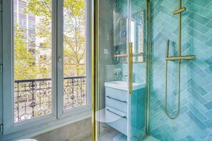 Ein Badezimmer mit Duschkabine aus Glas, einem weißen Waschbecken und einer Wand mit Fischgrätmuster.