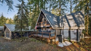 Mökki, jossa on puinen terassi, katettu kuisti ja metallikatto, ja sen ympärillä on tiheää metsää.