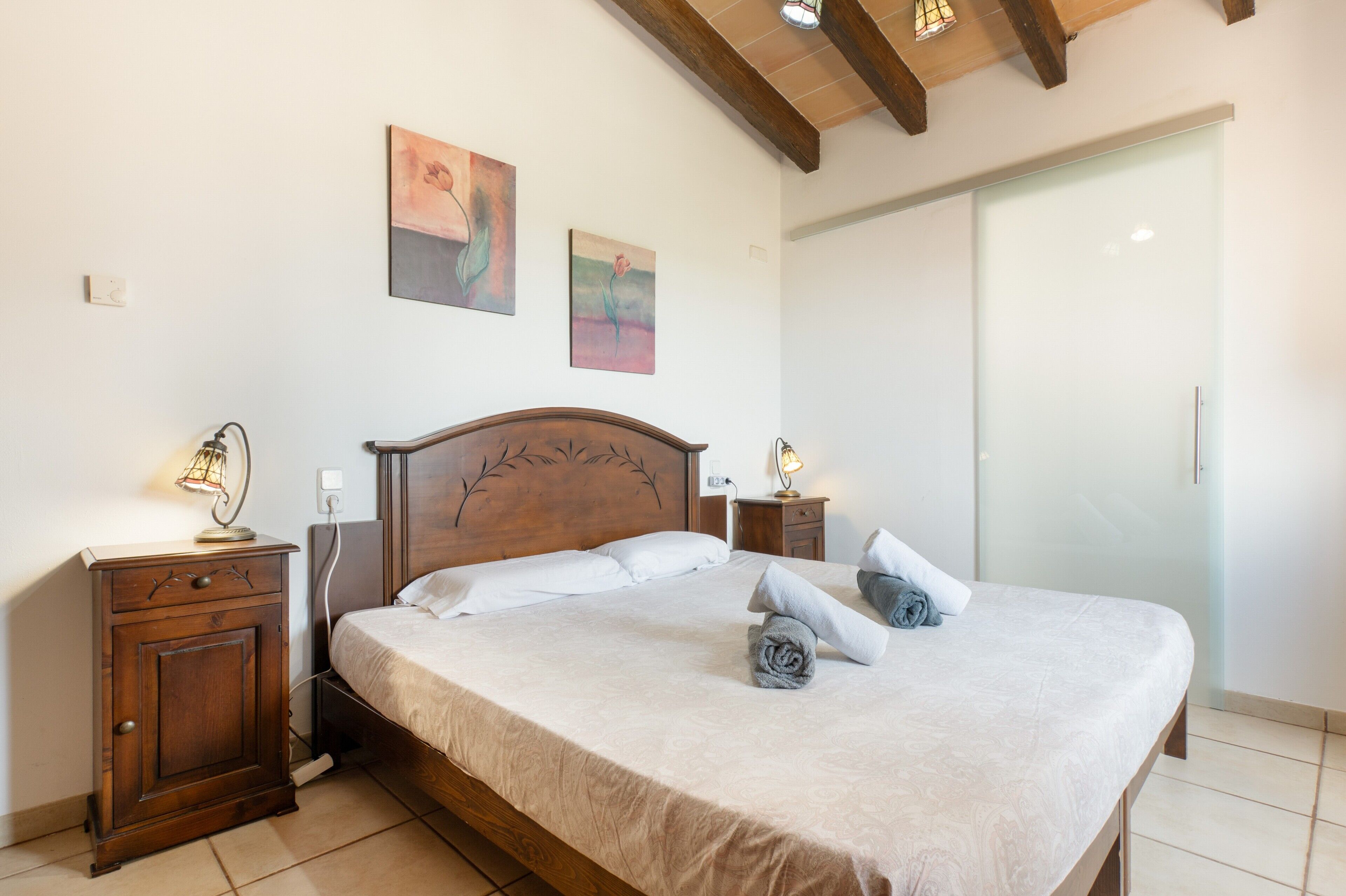 A bedroom with a wooden bed, bedside lamps, a nightstand, and two wall-mounted paintings.