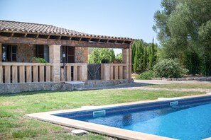 A poolside view of a building with a tiled roof, stone walls, and a wooden pergola. - Villas2meet Son Segarut: Perfect Family Villa Near Manacor in a Natural Setting (Manacor)