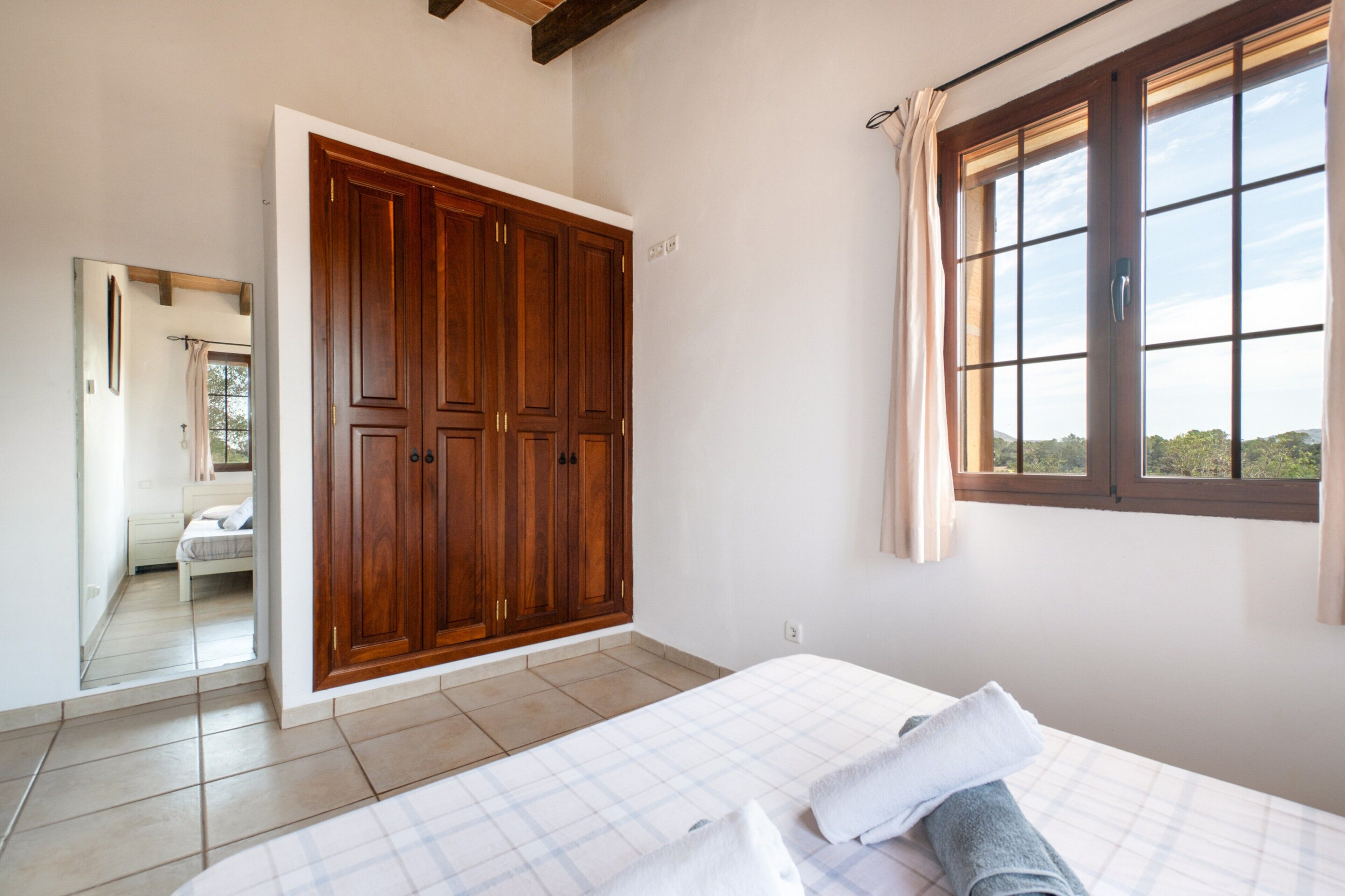 Ein Schlafzimmer mit Bett, großem Kleiderschrank, Fenster mit Aussicht und angrenzendem Badezimmer.