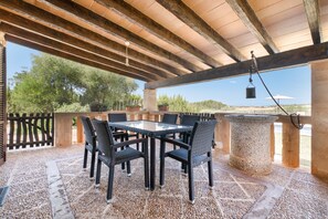 An outdoor patio with a table and chairs, a stone pillar, and a view of the landscape. - Villas2meet Son Segarut: Perfect Family Villa Near Manacor in a Natural Setting (Manacor)
