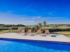 Un espace aménagé au bord de la piscine, avec des chaises longues et une vue sur la campagne.