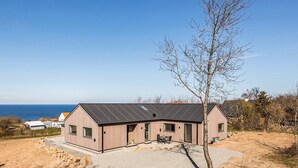 Une maison moderne avec un toit en pente, de grandes fenêtres et une vue sur la mer.