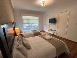 Ein Hotelzimmer mit zwei Betten, einem Fernseher, einem Fenster mit Jalousien und einer Deckenleuchte.