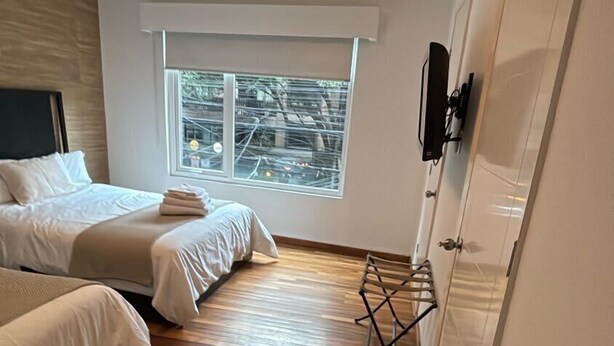 A bedroom with two beds, a wooden floor, a window with a view of trees, and a wardrobe. - Arquimedes Calm - Lovely 1BR in Polanco (Mexico City)