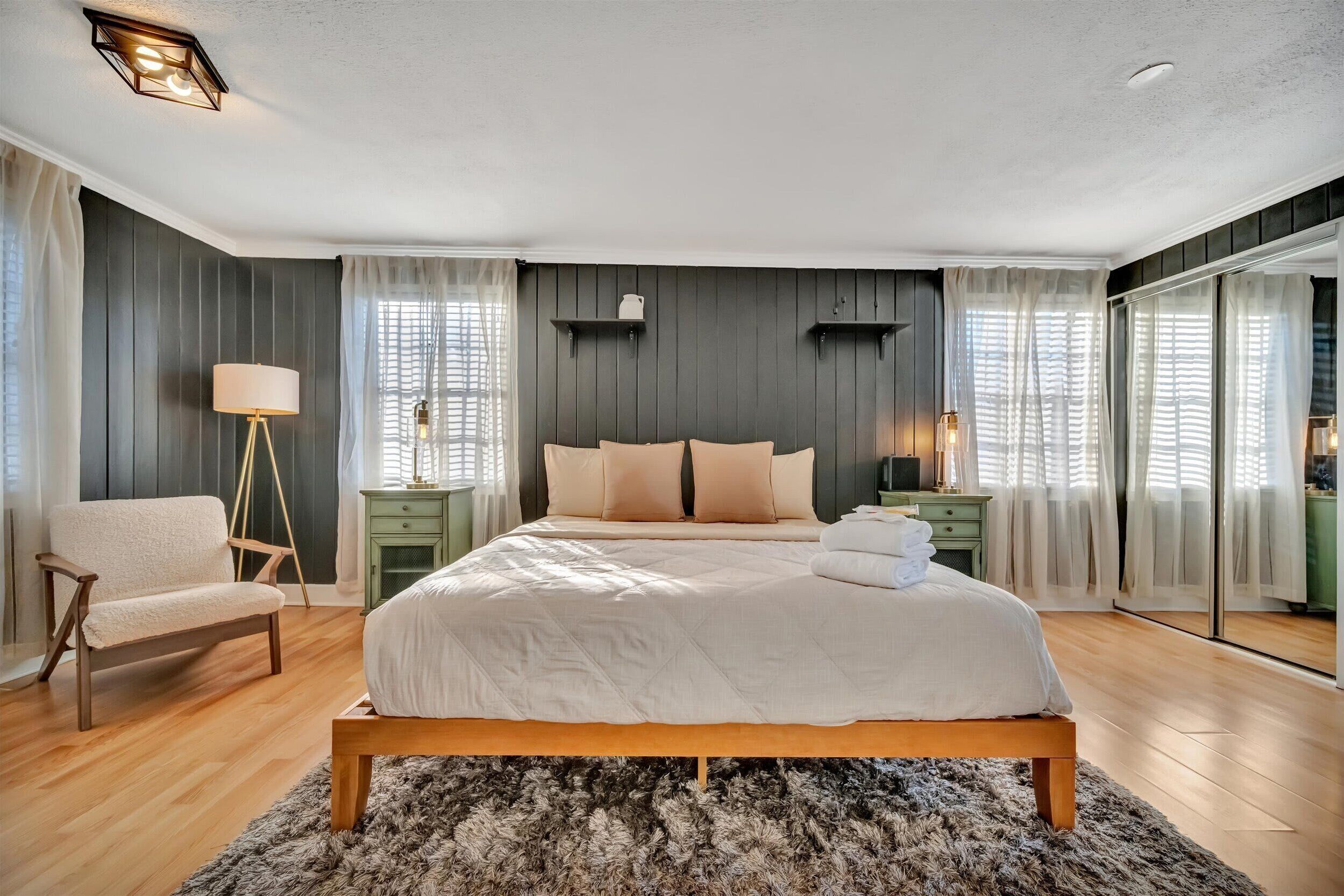A modern bedroom with a large bed, a chair, a floor lamp, and a bedside table.