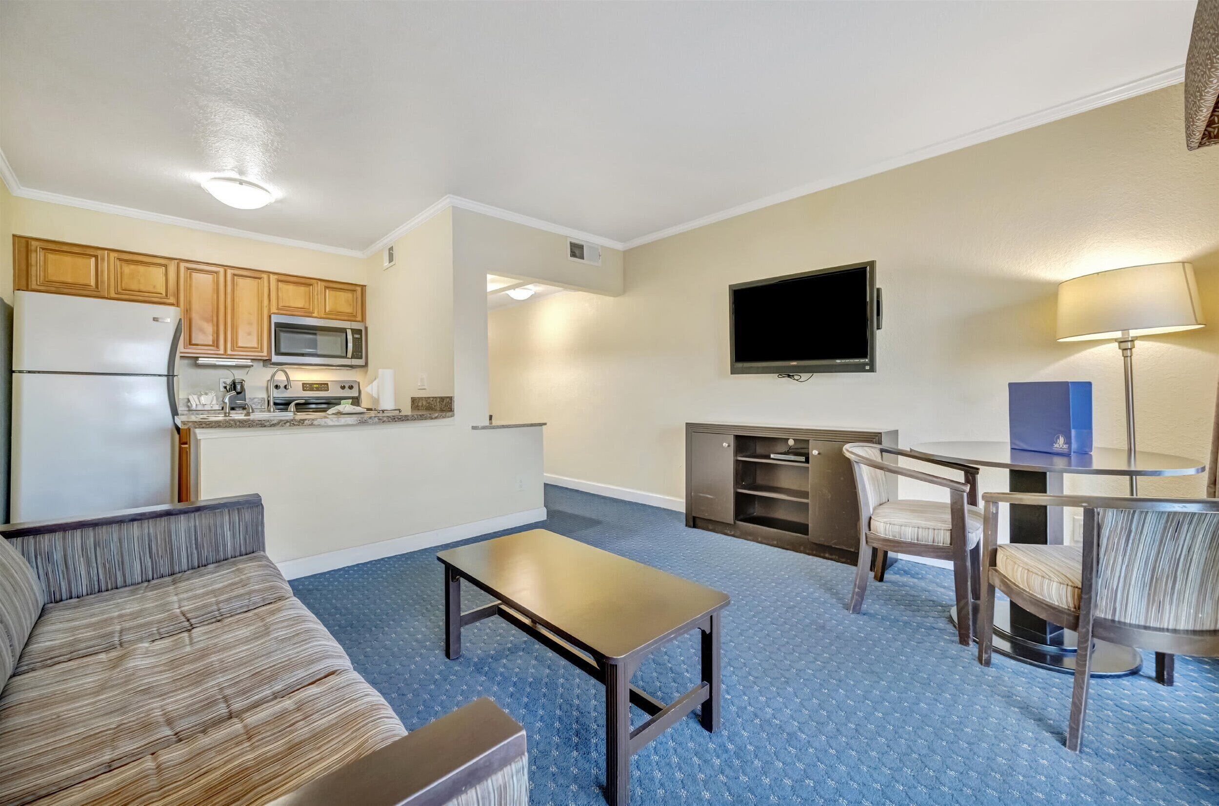 Un espacio habitable compacto con kitchenette, un televisor de pantalla plana, un sofá, una mesa de centro y una zona de comedor con sillas.