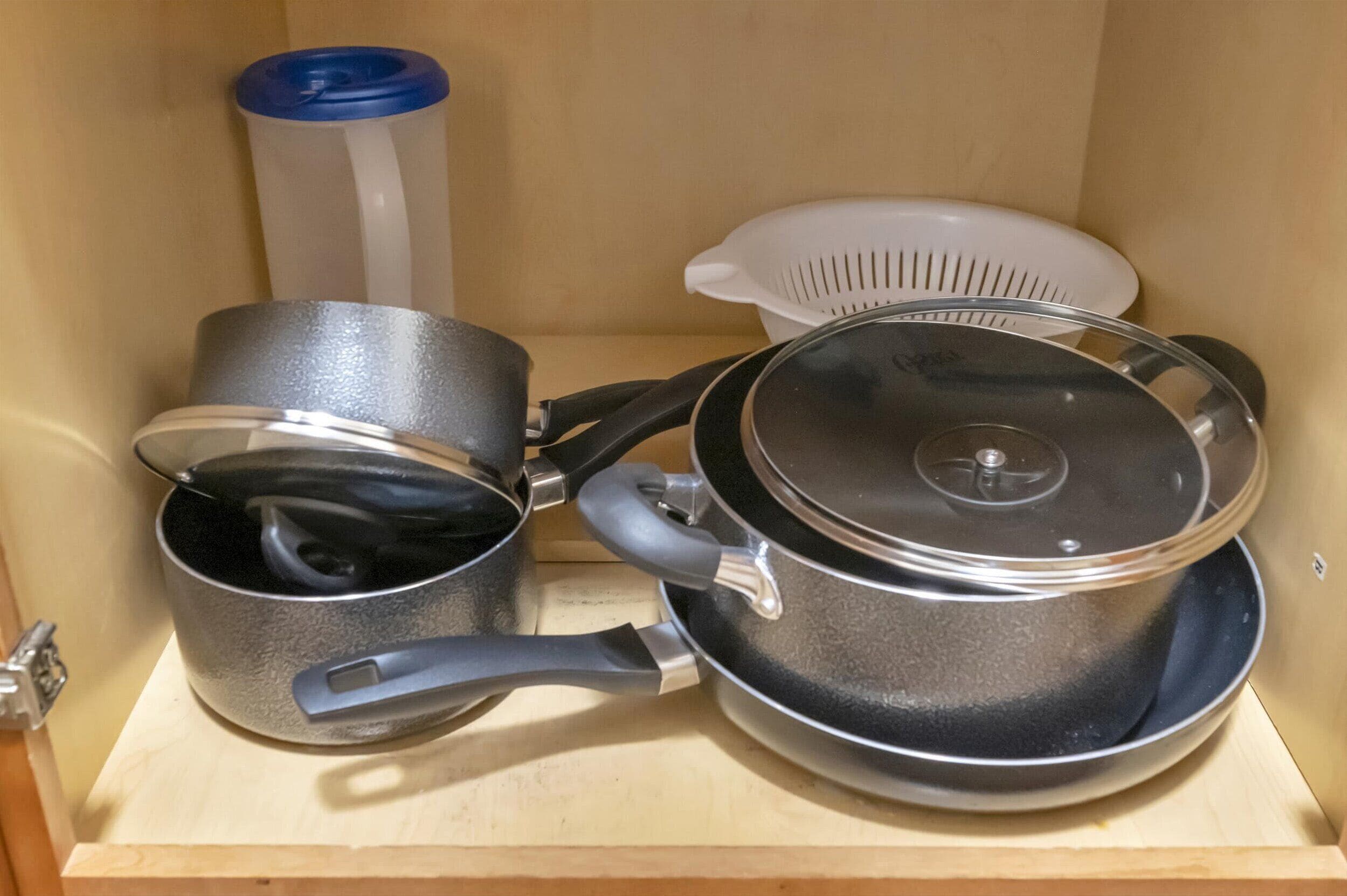 A kitchen cabinet with three pots and a colander.