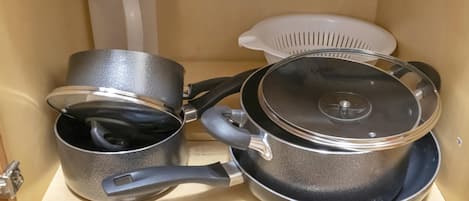 A kitchen cabinet with three pots and a colander.