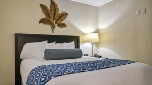 Camera d'albergo con un letto grande, un comodino, una lampada e una foglia decorativa a parete.