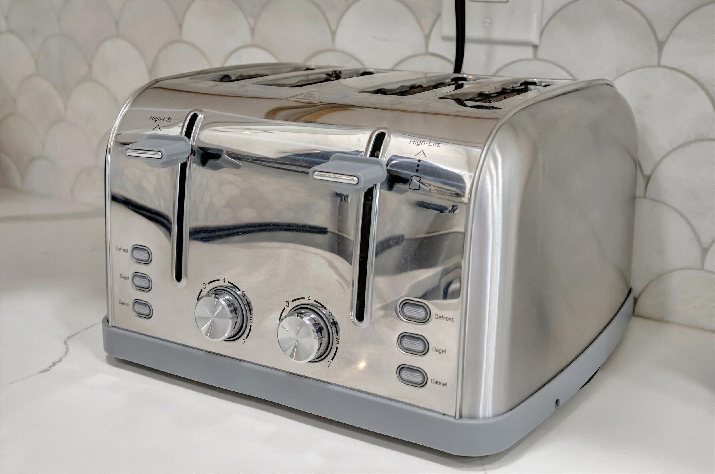 A stainless steel toaster with a control panel, placed on a white countertop.