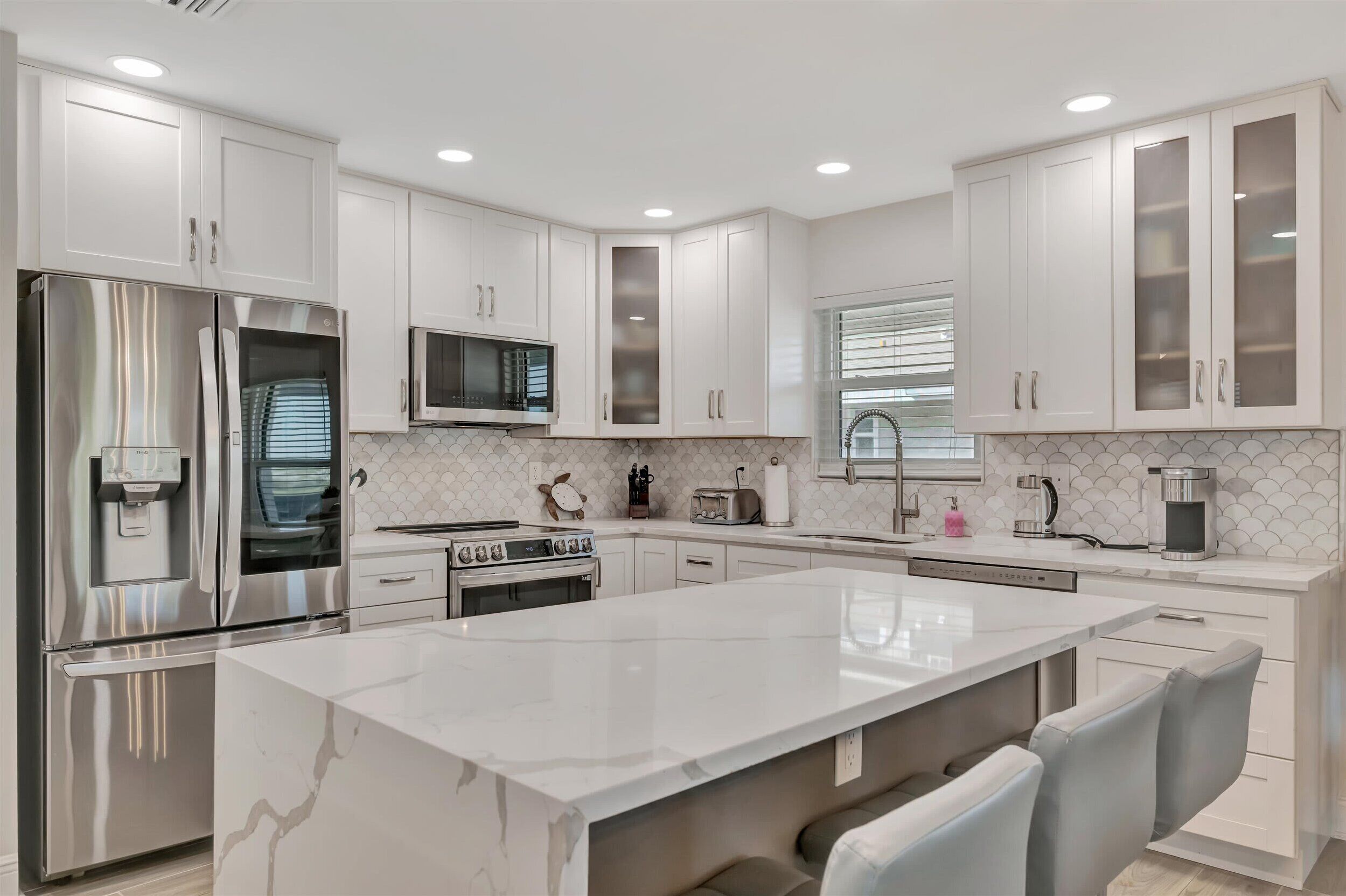 A modern kitchen with white cabinetry, stainless steel appliances, and a marble island.