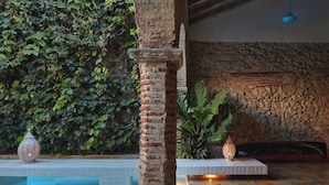 A pool area with a stone pillar, tiled flooring, and a stone wall with greenery. - NOK Award Winning 4BR Villa wih Pool at Getsemani (Cartagena)