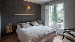 Un dormitorio con una cama grande, una mesita de noche, una lámpara y una ventana con cortinas.