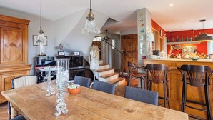 Una cocina amplia con armarios de madera, un comedor con una gran mesa de madera y una escalera que conduce a otro nivel.