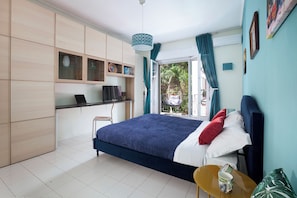 Un dormitorio con cama, escritorio y silla. Tiene una ventana con cortinas y una lámpara colgante.