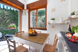 Una cocina con una mesa de madera, armarios blancos y una ventana con vista a la vegetación.
